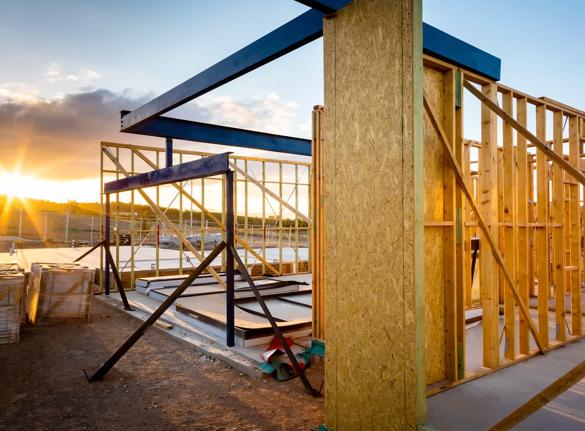 Timber-framed building under construction with blue structural steel beams at sunset